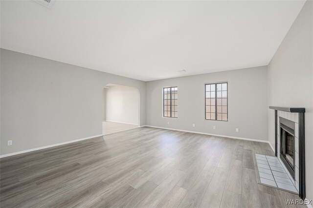 unfurnished living room with light wood finished floors, baseboards, arched walkways, and a tiled fireplace