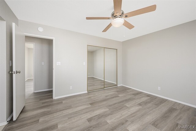 unfurnished bedroom featuring light wood-style floors, a closet, baseboards, and a ceiling fan