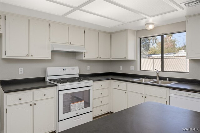 kitchen with dark countertops, white cabinetry, a sink, white appliances, and under cabinet range hood