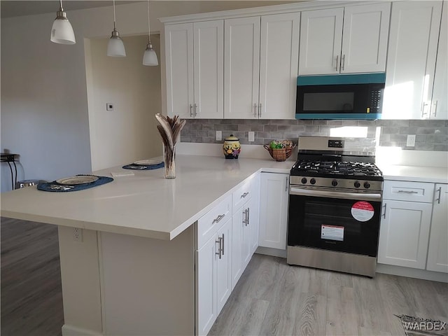 kitchen featuring decorative light fixtures, light countertops, white cabinetry, and stainless steel gas range oven