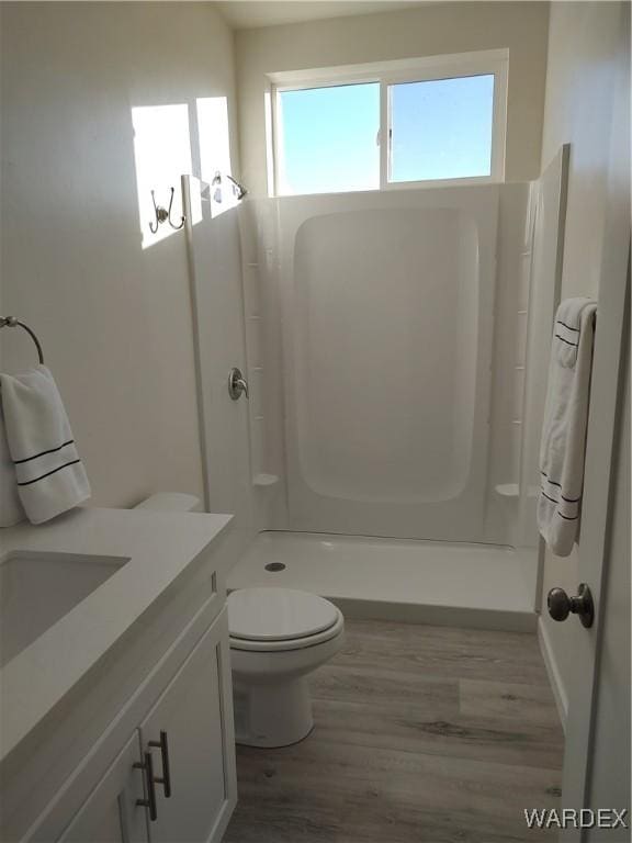 bathroom with toilet, walk in shower, wood finished floors, and vanity