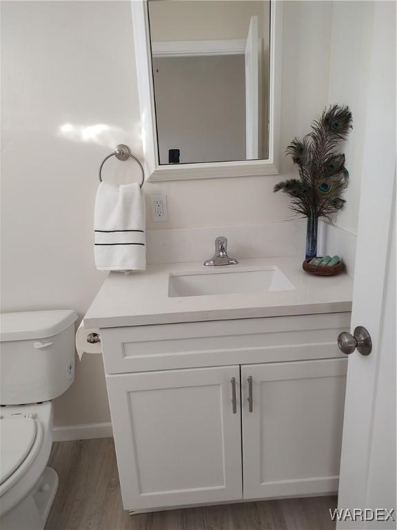 bathroom with toilet, wood finished floors, vanity, and baseboards