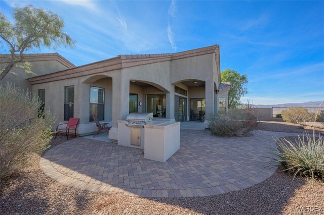 back of house with stucco siding, an outdoor kitchen, and a patio