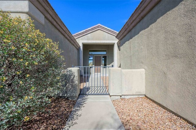 view of exterior entry featuring fence, a gate, and stucco siding