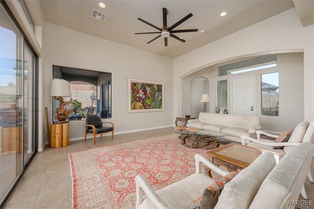 living area with light tile patterned floors, arched walkways, a ceiling fan, visible vents, and baseboards