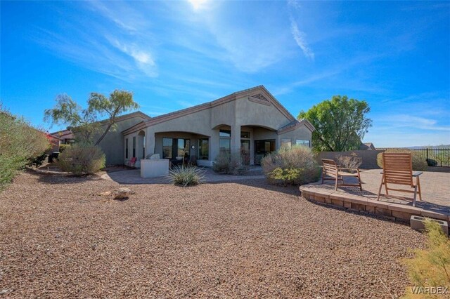 rear view of house featuring stucco siding, fence, and a patio