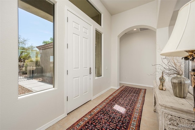 entryway with light tile patterned floors, arched walkways, and baseboards