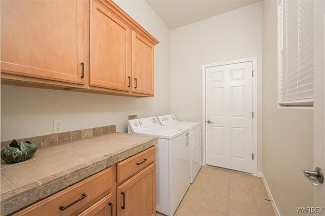 laundry room with cabinet space, independent washer and dryer, baseboards, and light tile patterned floors