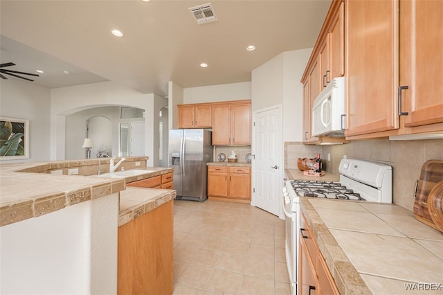 kitchen featuring white appliances, tasteful backsplash, visible vents, a ceiling fan, and a sink