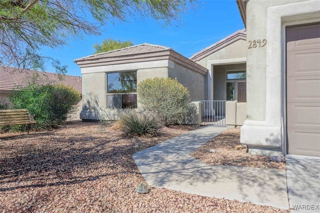 view of exterior entry with fence, a gate, and stucco siding