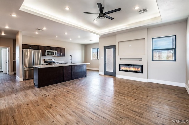 kitchen with visible vents, stainless steel appliances, a raised ceiling, and a kitchen island with sink