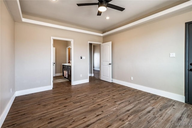 unfurnished bedroom with dark wood-style floors, recessed lighting, a raised ceiling, connected bathroom, and baseboards