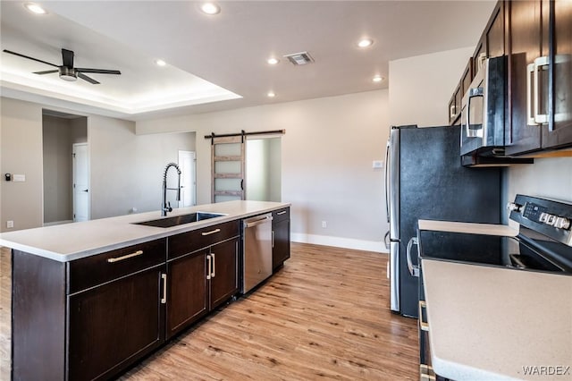 kitchen with a barn door, an island with sink, appliances with stainless steel finishes, light countertops, and a sink