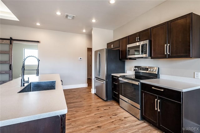 kitchen featuring stainless steel appliances, light countertops, visible vents, a barn door, and a sink