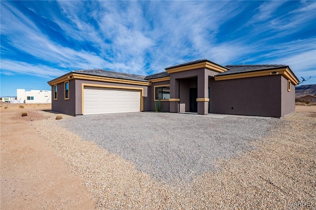 view of front of property featuring stucco siding, an attached garage, and gravel driveway