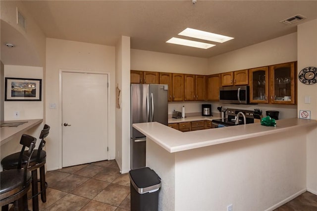 1650 Smoketree Ave Unit 103, Lake Havasu, AZ 86403 - kitchen with stainless steel appliances, brown cabinetry, glass insert cabinets, a peninsula, and light countertops
