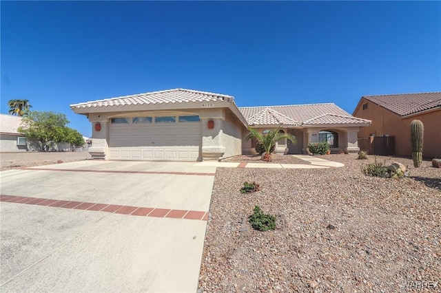 mediterranean / spanish house with an attached garage, a tiled roof, concrete driveway, and stucco siding