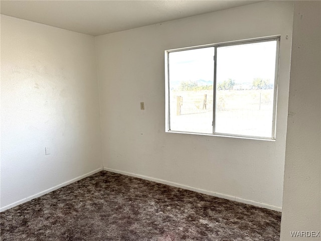 unfurnished room with baseboards and dark colored carpet