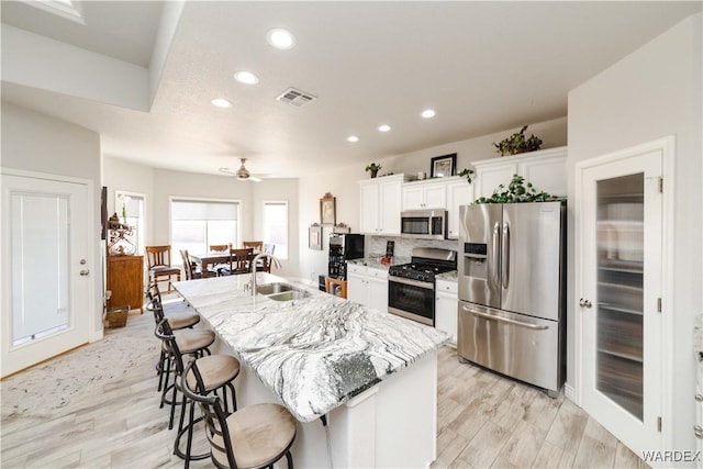 kitchen featuring white cabinets, light stone counters, a kitchen island with sink, stainless steel appliances, and a sink