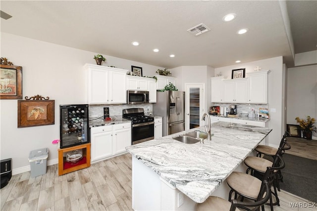 kitchen featuring a breakfast bar, stainless steel appliances, visible vents, white cabinetry, and a sink