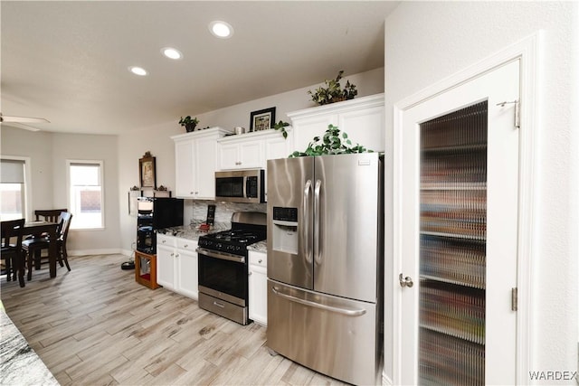 kitchen with light stone counters, light wood-style flooring, recessed lighting, stainless steel appliances, and white cabinetry