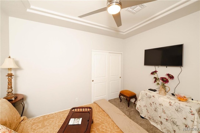 carpeted bedroom with a tray ceiling, a closet, visible vents, and a ceiling fan