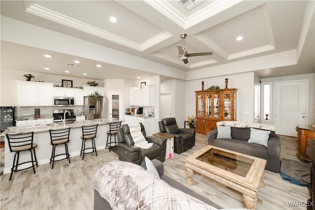 living area with ornamental molding, coffered ceiling, visible vents, and light wood finished floors