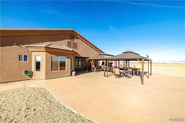 rear view of property featuring a tile roof, a patio, a gazebo, and stucco siding