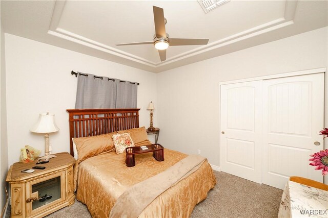 bedroom with a closet, light colored carpet, a raised ceiling, and visible vents