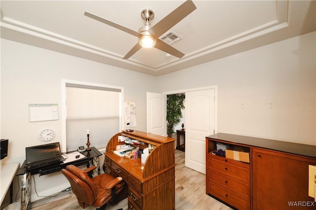 office space with light wood-style floors, a tray ceiling, visible vents, and ceiling fan