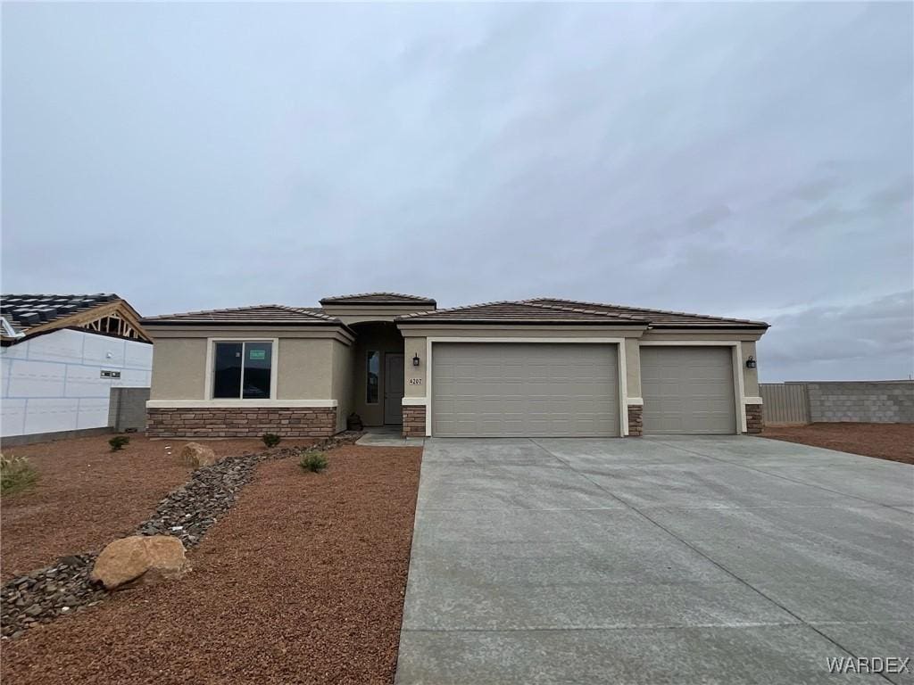 prairie-style house with an attached garage, stone siding, driveway, and stucco siding