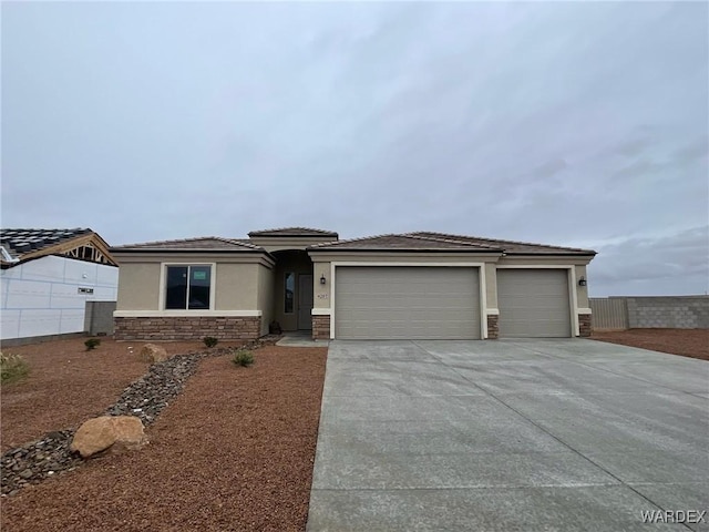 prairie-style house with an attached garage, stone siding, driveway, and stucco siding