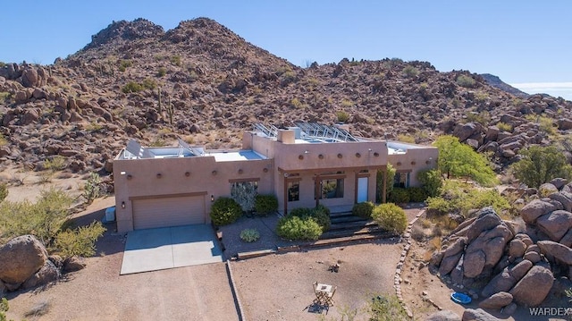 pueblo-style house featuring a garage, a mountain view, driveway, and stucco siding