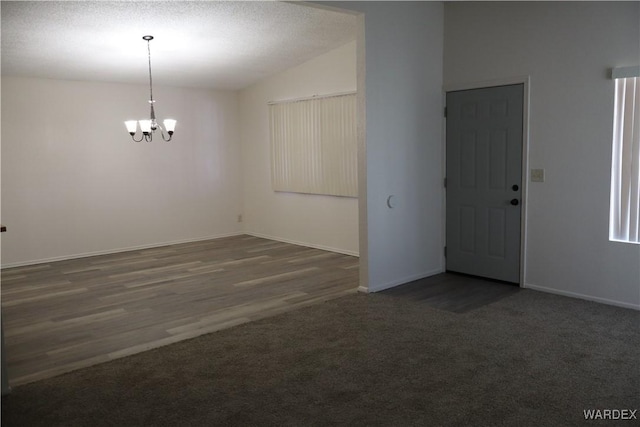 empty room with baseboards, dark carpet, vaulted ceiling, a textured ceiling, and a chandelier