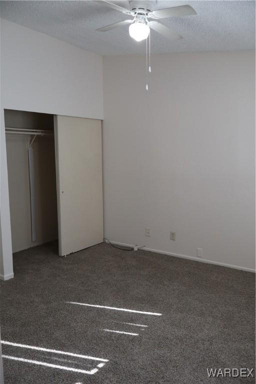 unfurnished bedroom with a textured ceiling, dark colored carpet, a closet, and a ceiling fan