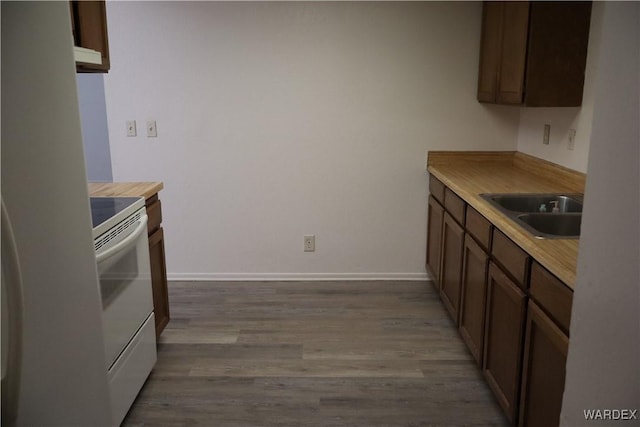 kitchen featuring electric range, baseboards, light countertops, light wood-style floors, and a sink