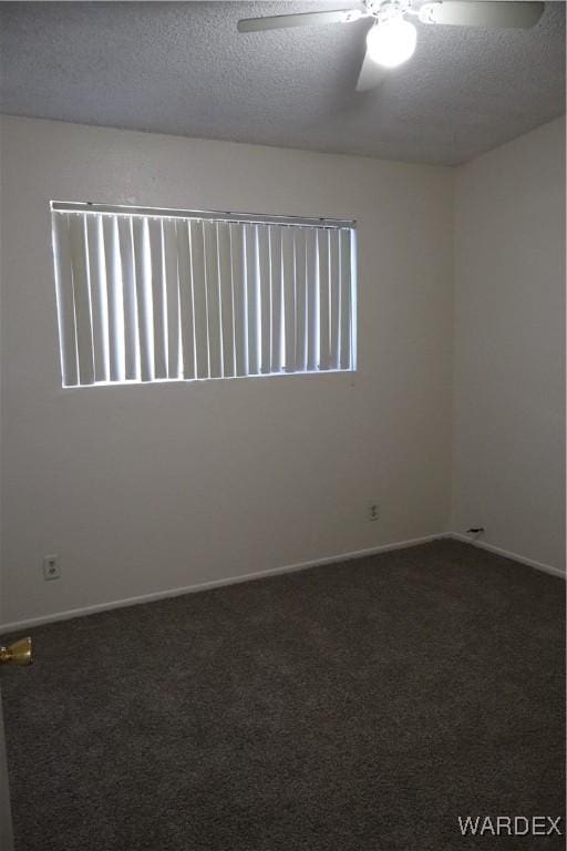 spare room featuring dark colored carpet, ceiling fan, a textured ceiling, and baseboards