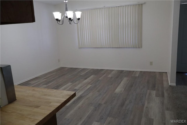 unfurnished dining area with a chandelier, wood finished floors, and baseboards