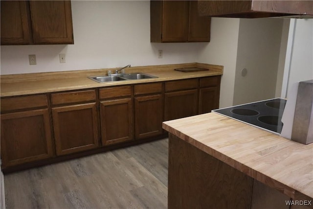 kitchen with light wood-style flooring, dark brown cabinets, a sink, and stovetop