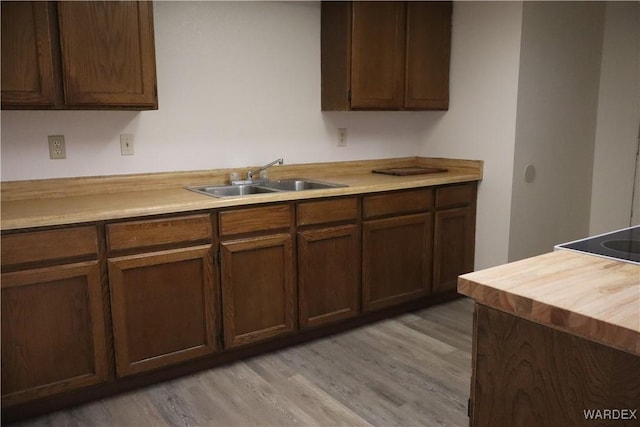 kitchen featuring dark brown cabinetry, light wood-style flooring, and a sink