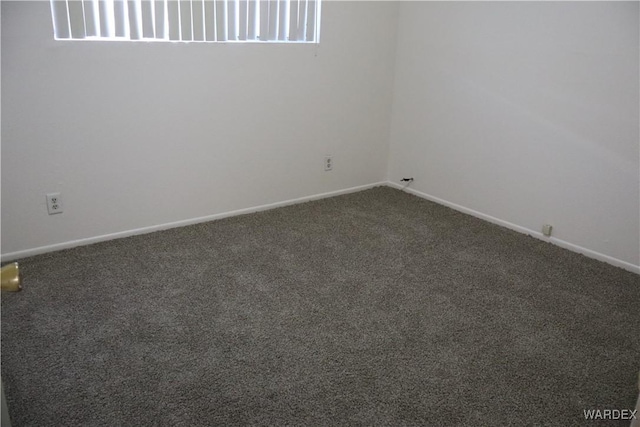 spare room with dark carpet and baseboards