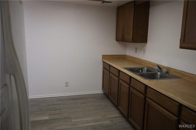 kitchen with light countertops, a sink, dark brown cabinets, light wood-type flooring, and baseboards