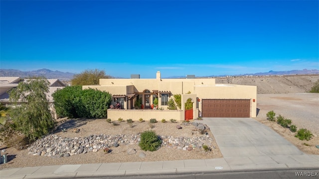 pueblo-style house featuring driveway, a garage, a mountain view, and stucco siding