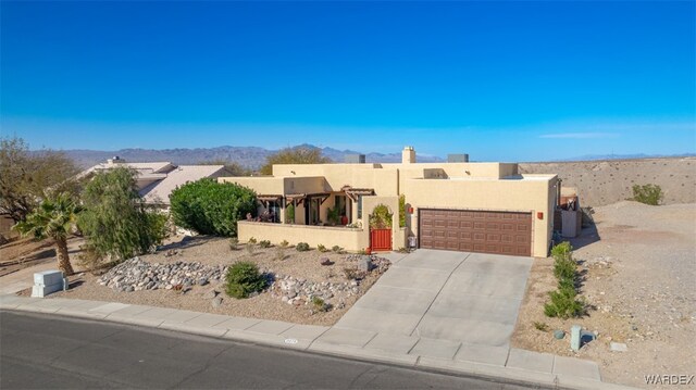 pueblo-style house featuring concrete driveway, an attached garage, a mountain view, and stucco siding