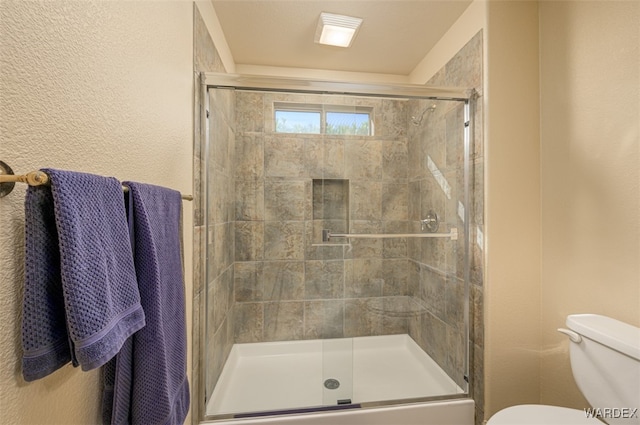 bathroom featuring a textured wall, a stall shower, and toilet