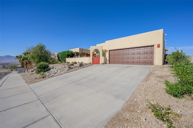 southwest-style home with concrete driveway, an attached garage, fence, a mountain view, and stucco siding