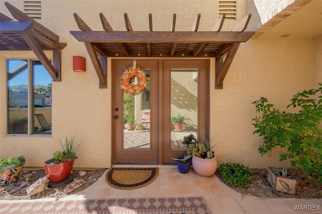 view of exterior entry featuring a patio area, a pergola, french doors, and stucco siding