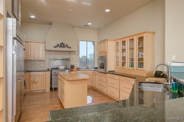 kitchen featuring premium range hood, a sink, appliances with stainless steel finishes, a center island, and glass insert cabinets