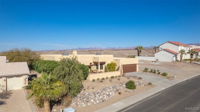 pueblo-style house with a mountain view, a garage, fence, a residential view, and stucco siding