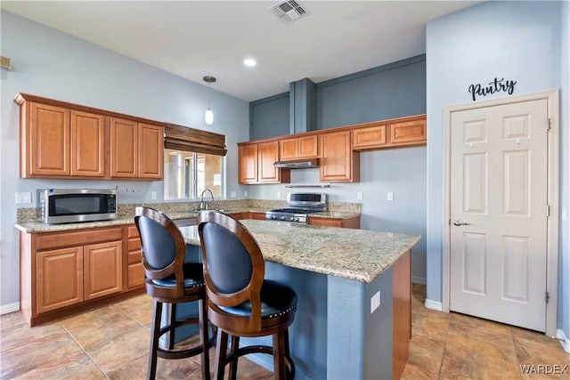 kitchen featuring visible vents, brown cabinets, a center island, light stone countertops, and stainless steel appliances